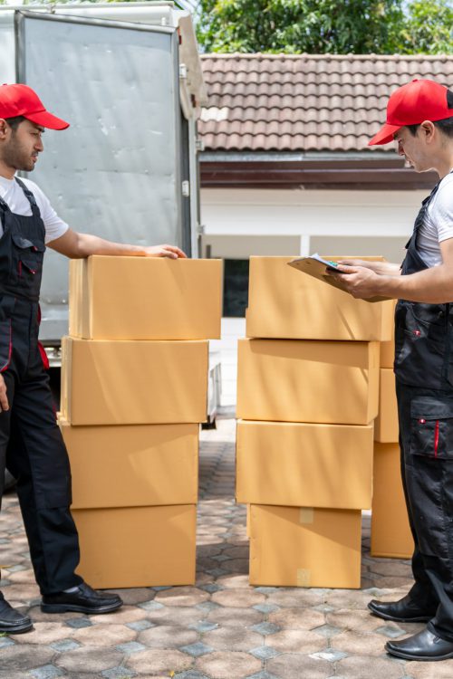 Caucasian delivery man checking a list of delivering package in truck. Attractive courier postman worker team in uniform working and preparing to load deliver box cardboard postal from car van.